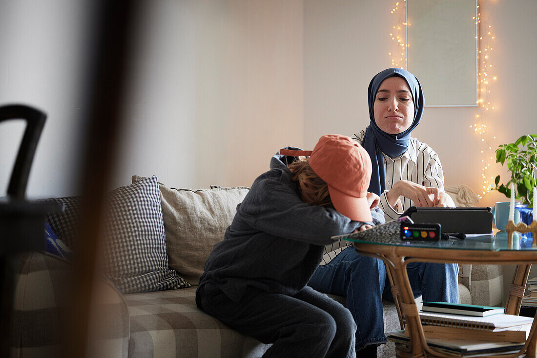 Mutter mit Hidschab hilft müdem Sohn mit ADS oder ADHS bei den Hausaufgaben