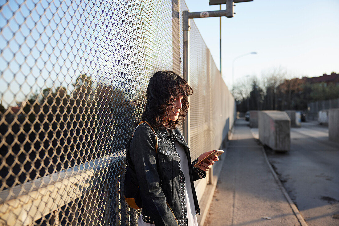 Young woman leaning on fence and using cell phone