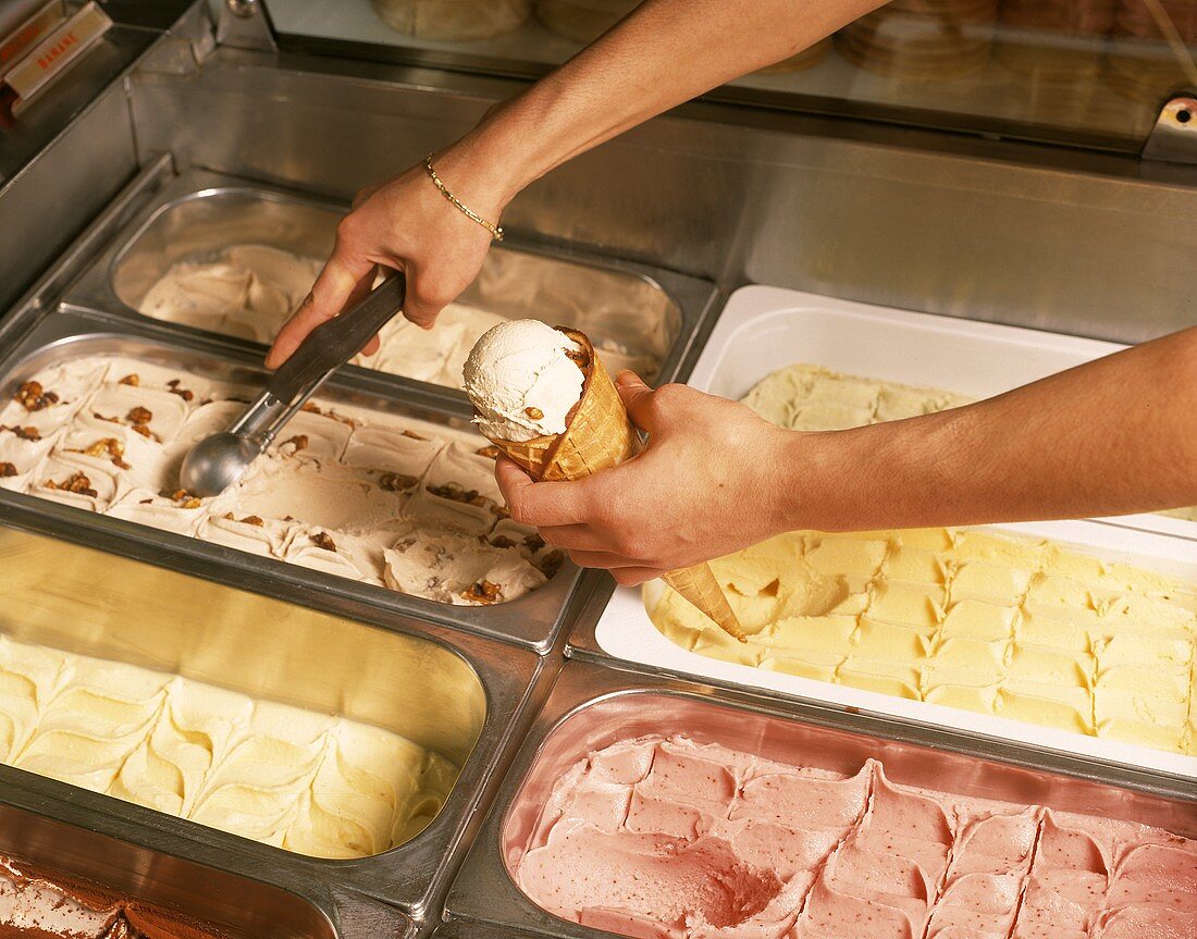Filling ice cream cone from ice cream containers with scoop
