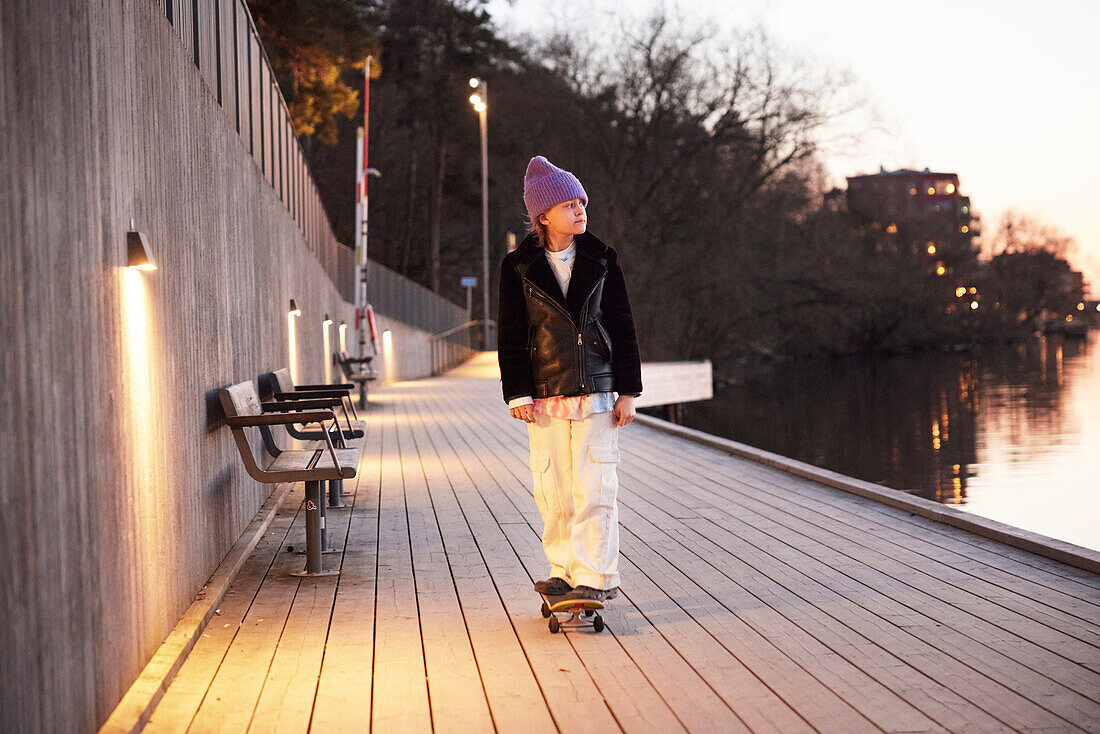 Young boy skateboarding at evening by the river and looking away