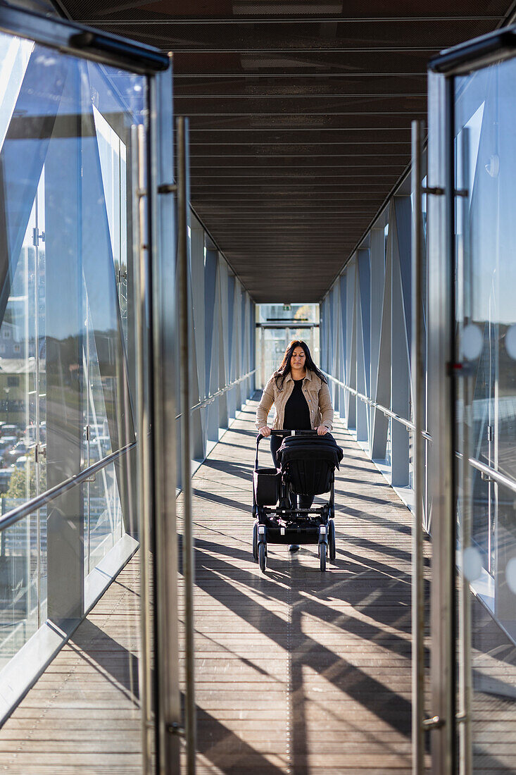 View of woman on parental leave pushing pram through elevated walkway