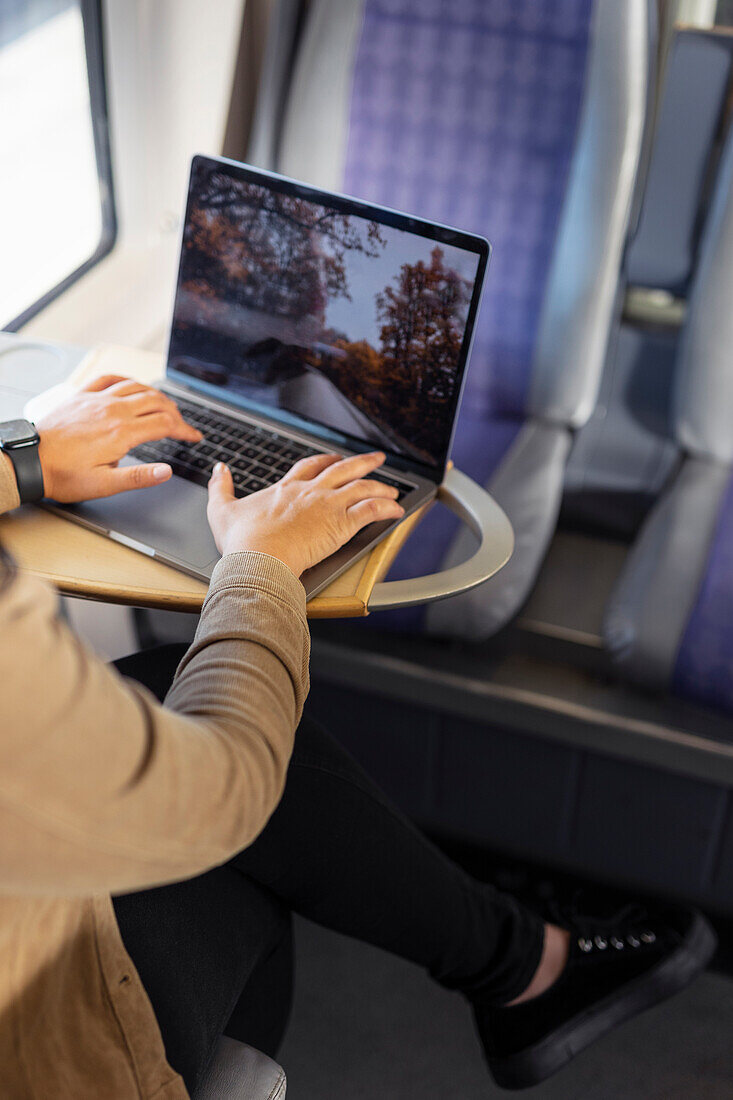 Mittlerer Ausschnitt einer Frau mit Laptop während einer Zugfahrt