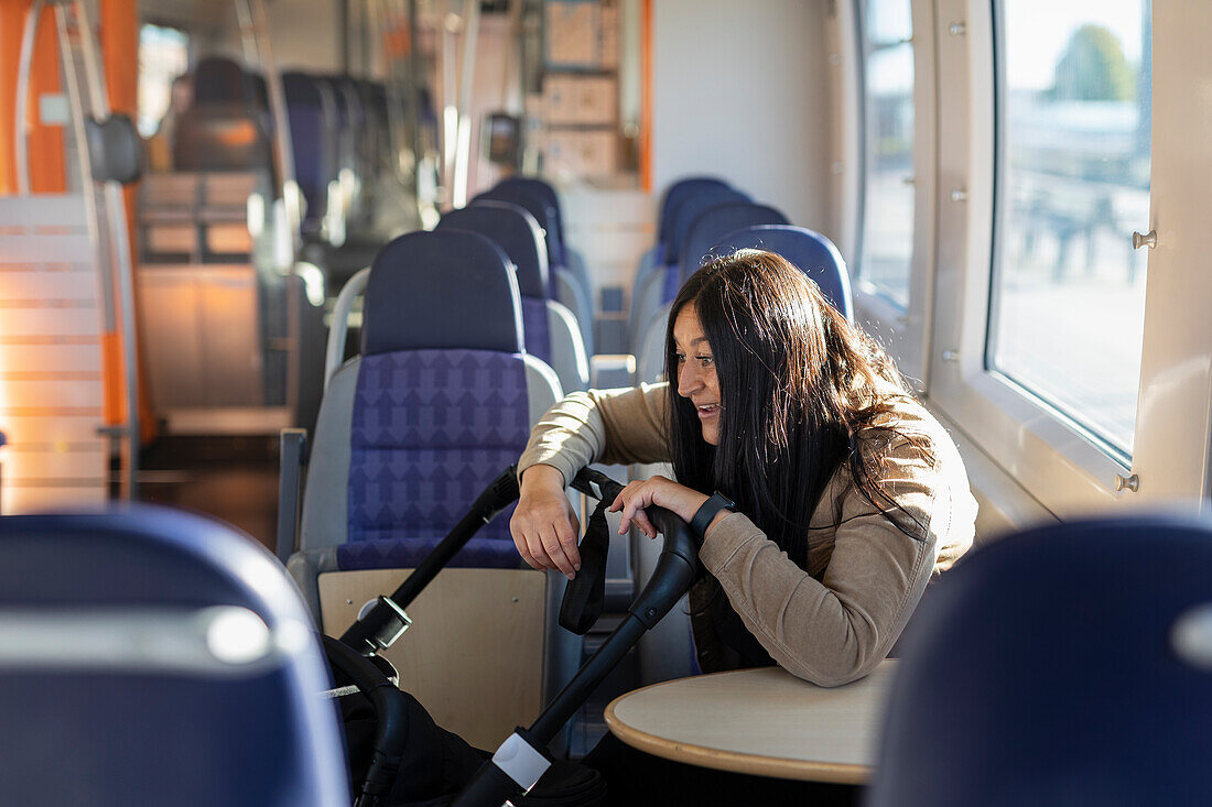 Lächelnde Frau im Erziehungsurlaub im Zug mit Blick auf Baby im Kinderwagen