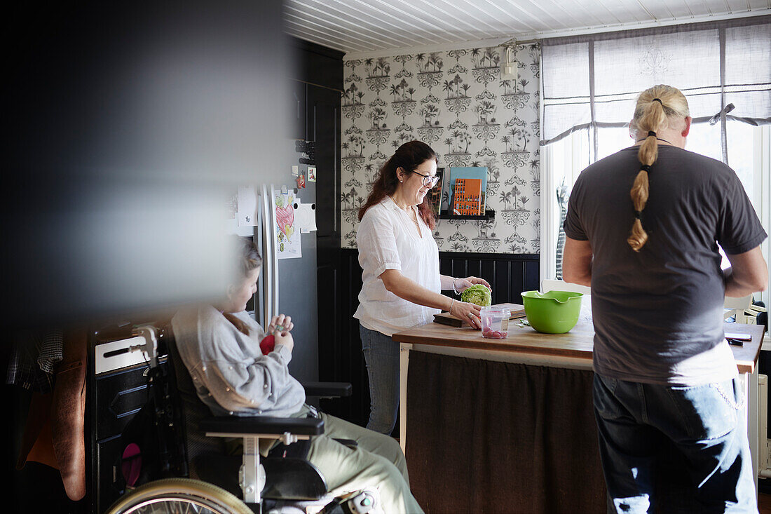 Eltern mit behinderter Tochter im Rollstuhl bei der Essenszubereitung in der Küche