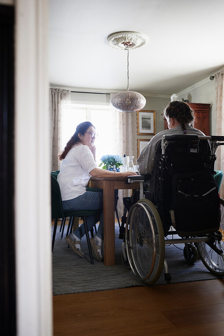 Mutter und behinderte jugendliche Tochter im Rollstuhl sitzen am Küchentisch
