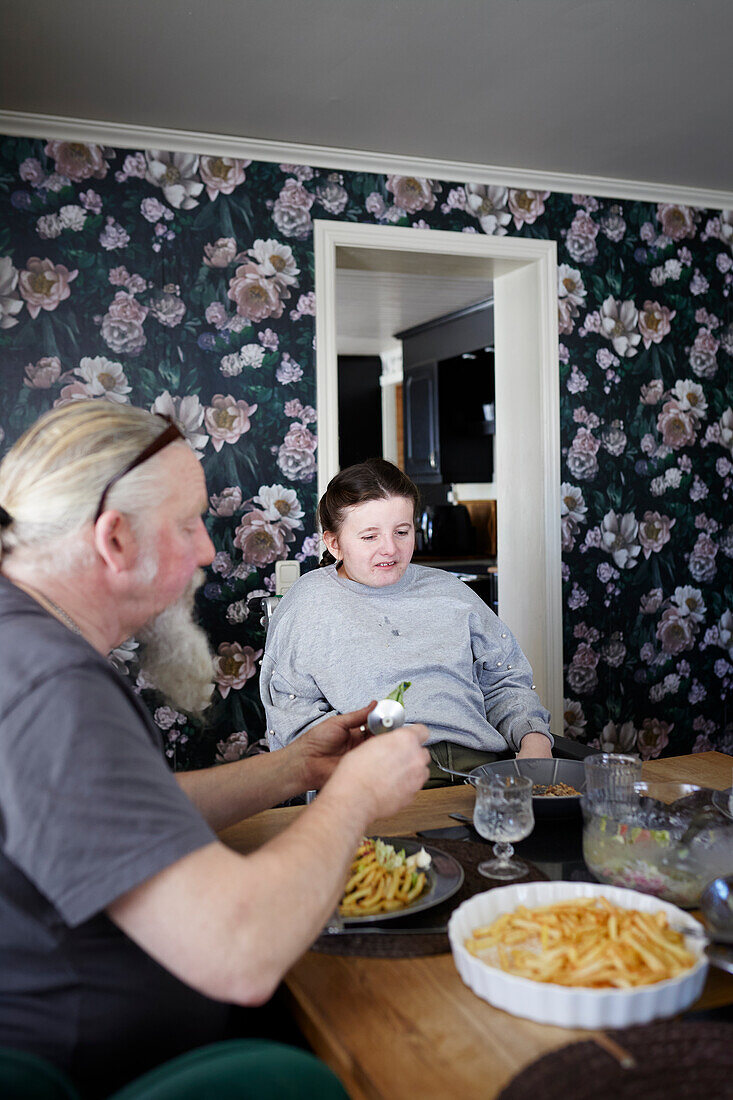 Father and disable teenage girl sitting and dining table and having meal