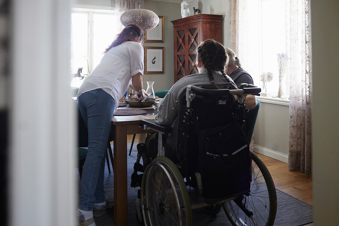 Eltern mit behinderter Tochter im Rollstuhl beim Essen am Esstisch