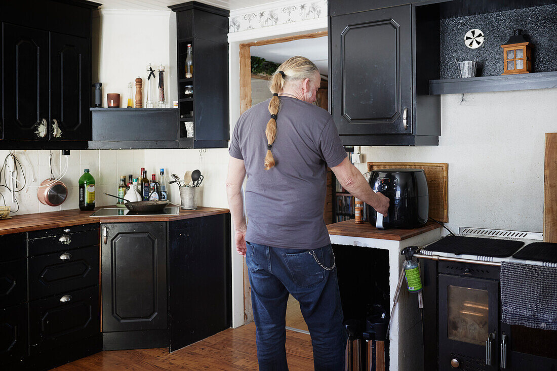 Älterer Mann bei der Benutzung einer Heißluftfritteuse in der Küche