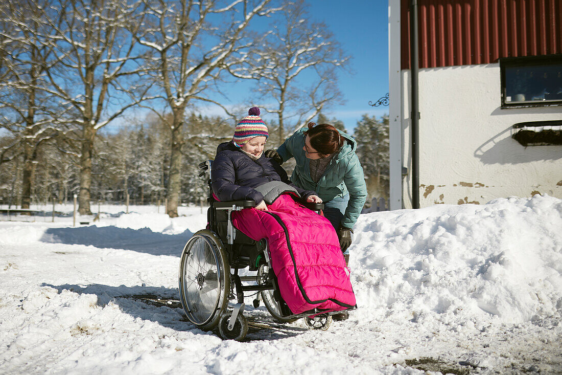 Mother talking to teenage daughter on wheelchair during winter walk