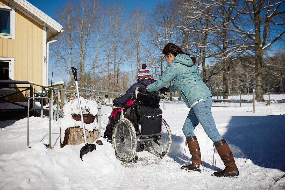 Rear view of woman pushing person on wheelchair during winter walk