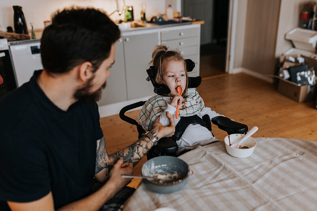 Father feeding disabled child in wheelchair at kitchen table