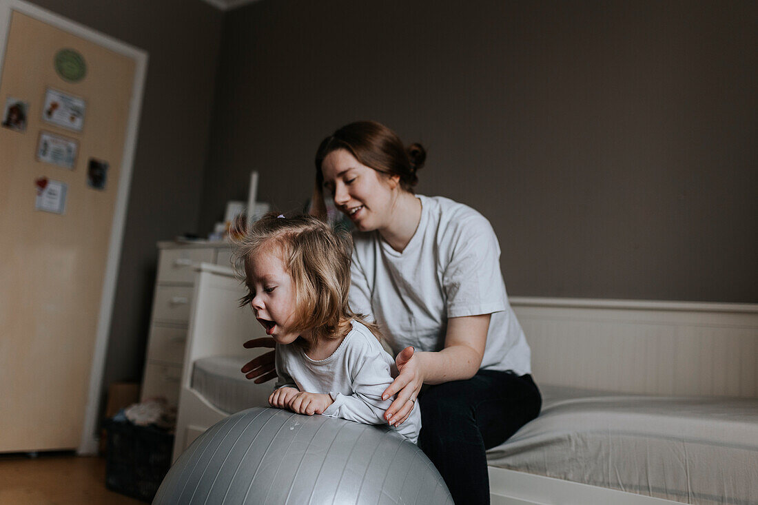 Mother supporting disabled child on fitness ball