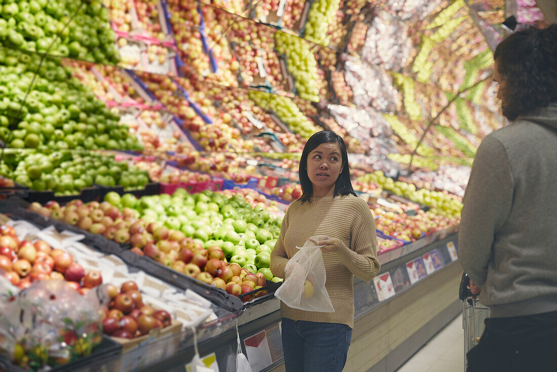 View of couple standing in supermarkets and talking while choosing apples