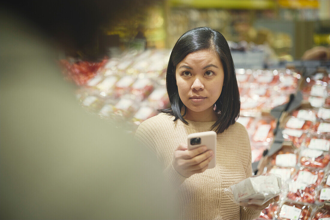 Frau steht im Supermarkt und hält Handy in der Hand