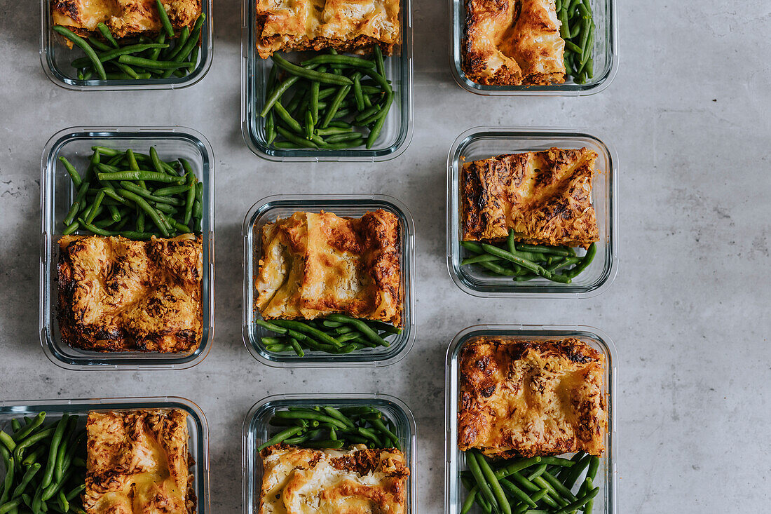 Overhead view of lunch boxes with lasagna and green beans as part of healthy meal prep