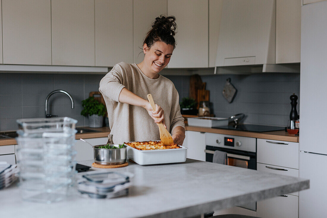 Glückliche Frau beim Portionieren von Lasagne als Teil der Essensvorbereitung
