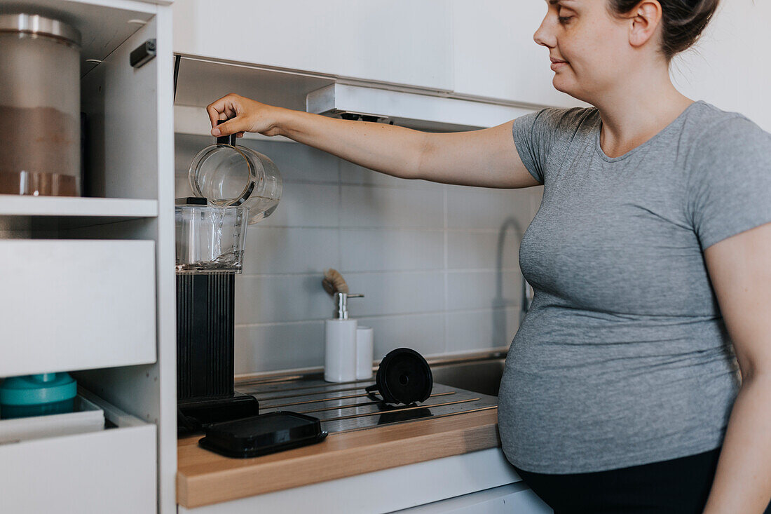 Pregnant woman preparing coffee in kitchen
