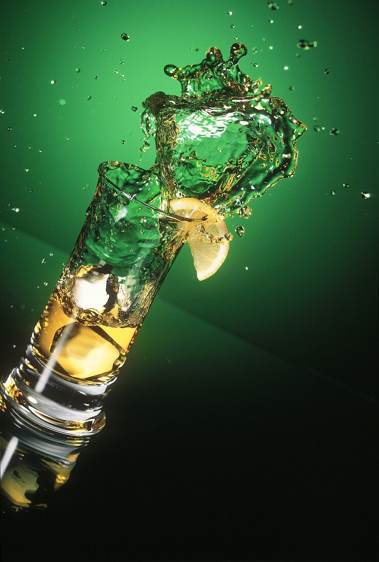 Eistee spritzt aus dem Glas, grüner Hintergrund