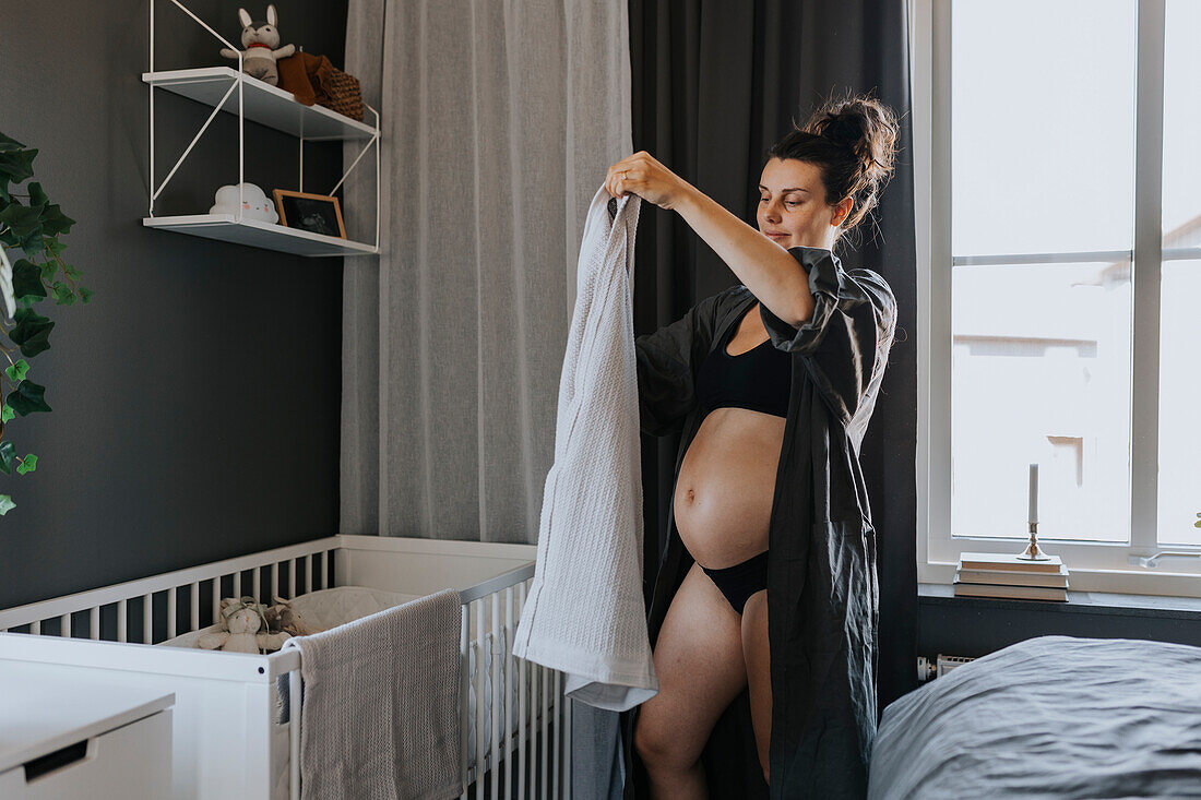Pregnant woman organizing baby crib and getting ready for baby arrival