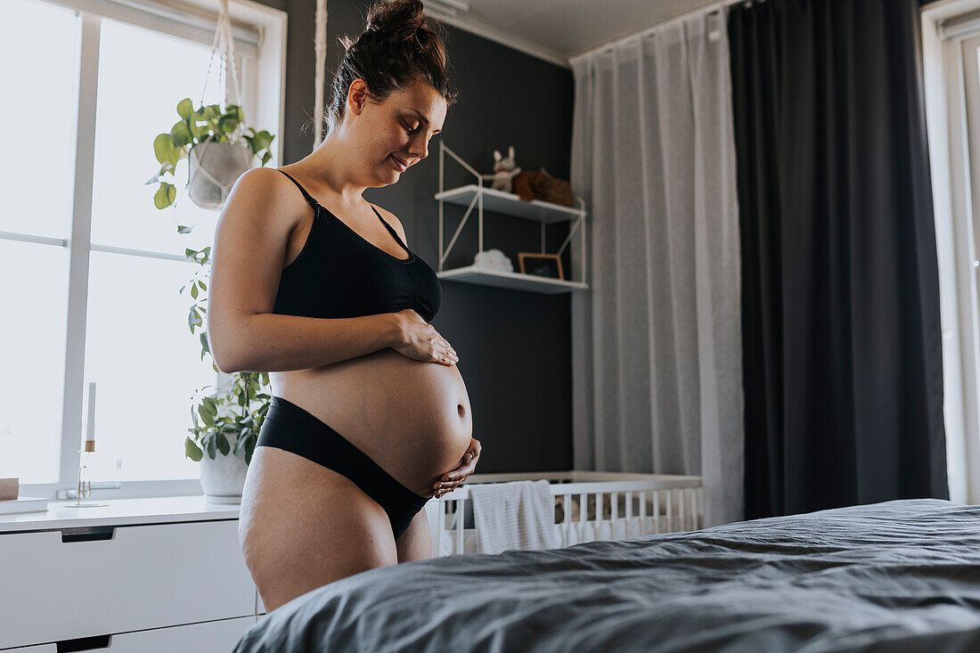 Schwangere Frau massiert Bauch im Schlafzimmer