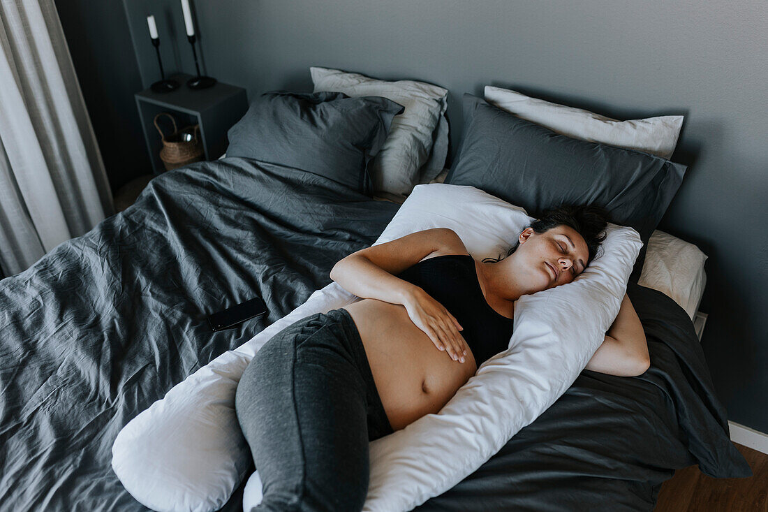 Schwangere Frau schläft auf einem Schwangerschaftskissen im Bett