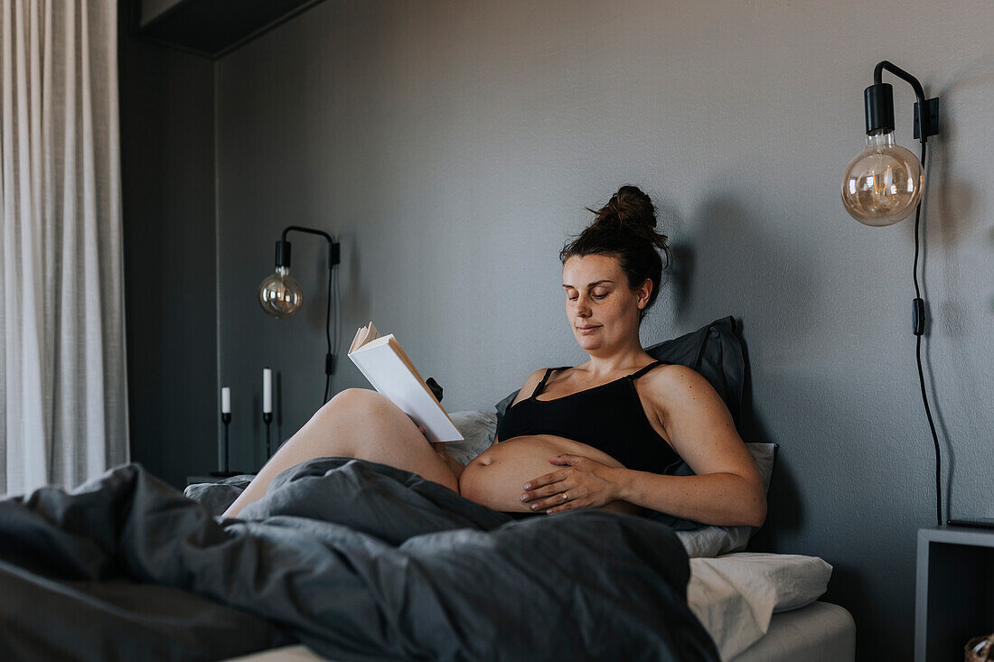 Schwangere Frau entspannt sich im Bett und liest ein Buch