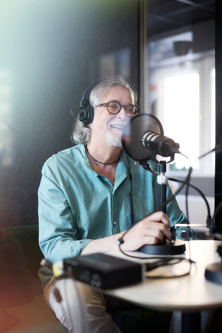 Reifer Mann sitzt und moderiert einen Podcast oder eine Radiosendung oder einen Podcast