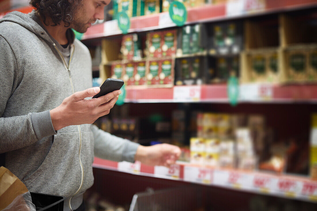 Mann im Supermarkt vergleicht Preise während der Inflation mit dem Handy