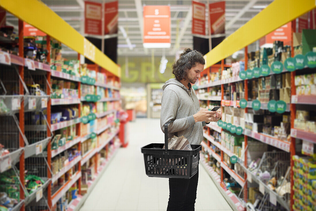 Mann im Supermarkt vergleicht Preise während der Inflation auf dem Handy