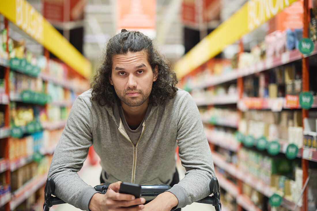 Mann im Supermarkt hält Handy und schaut in die Kamera