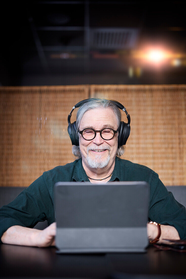Lächelnder älterer Mann mit Kopfhörern und Tablet