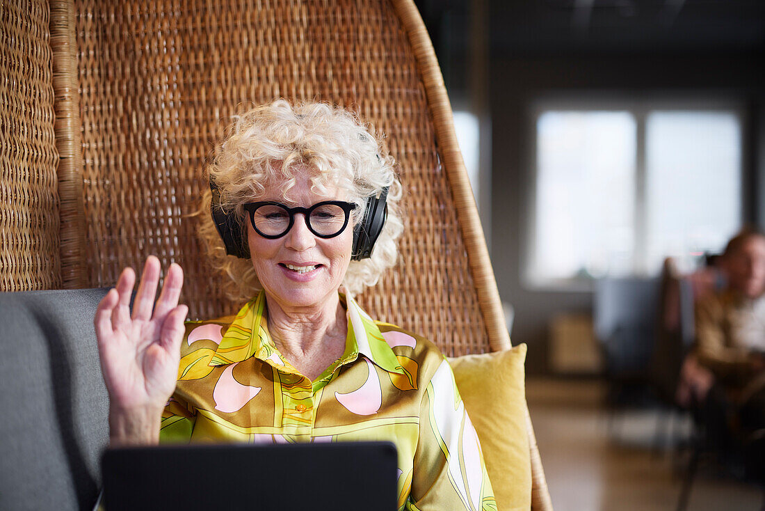 Ältere Frau mit Kopfhörern bei einem Videogespräch auf einem Tablet