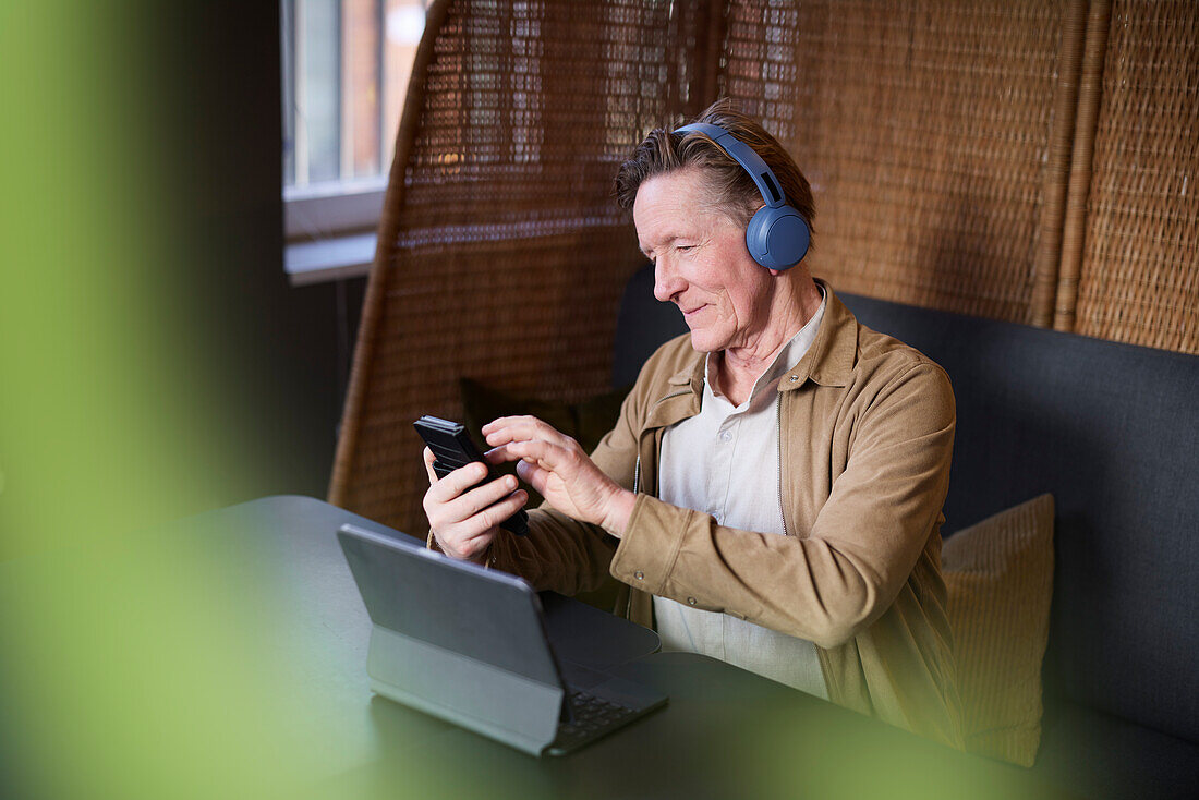 Senior man with headphones using phone and tablet