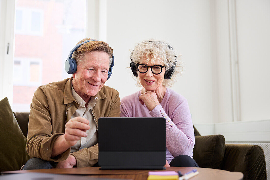 Älterer Mann und Frau sitzen im Wohnzimmer und verwenden ein digitales Tablet zur Bearbeitung eines Podcasts