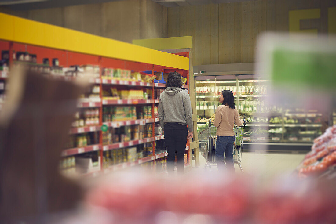 Rückansicht eines Paares, das im Supermarkt vor den Regalen steht und gemeinsam einkaufen geht