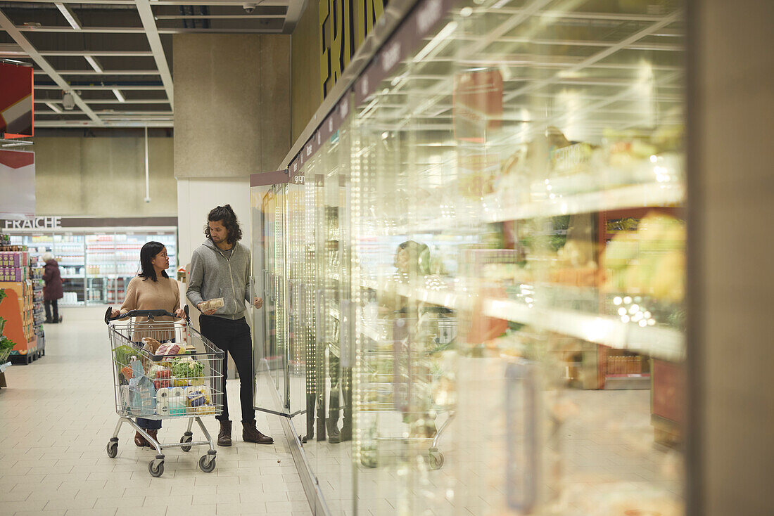 Couple in supermarket talking in front of fridges with vegetables