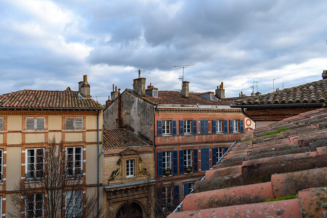 Alte Häuser in der Altstadt von Toulouse, Tondachziegel und eine Häuserreihe mit Fensterläden und geschnitzten Fenstereinfassungen aus Stein.