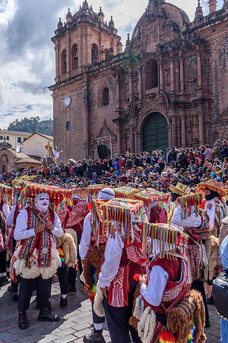 Cusco, a cultural fiesta, people dressed in traditional colourful costumes with masks and hats, brightly coloured streamers, in the Cusco central square by the cathedral. 