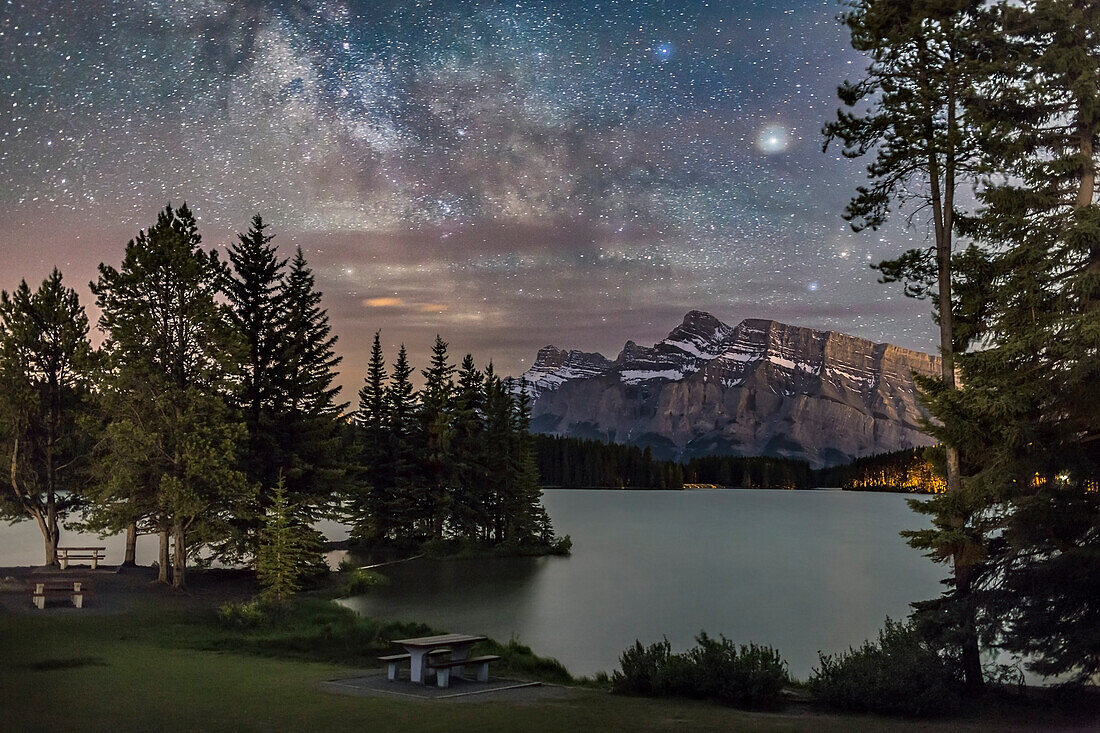 Die Milchstraße in Sagittarius und Skorpius, tief im Süden, über Mt. Rundle in Banff, Alberta, vom Ufer des Two Jack Lake aus, 3. Juni 2016. Saturn ist das helle Objekt oben rechts, dann in Ophiuchus direkt über Skorpion. Einige dünne Wolken haben die Bilder von Saturn und Sternen unscharf gemacht. Der Vordergrund wird teilweise von Autoscheinwerfern beleuchtet, um die grüne Landschaft zu erhellen. Der Wind machte das Wasser rau und unreflektiert.