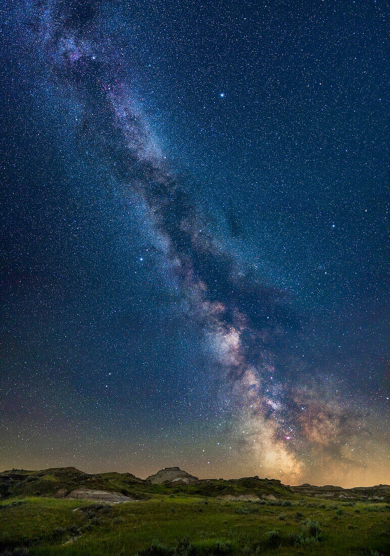 Dieses Bild zeigt den vertikalen Verlauf der sommerlichen Milchstraße über der Landschaft des Dinosaur Provincial Park, Alberta. Das Bild veranschaulicht den Reichtum an Objekten, dunklen Staubspuren und hellen Sternenfeldern entlang der Milchstraße, von Sagittarius tief im Süden unten bis Cygnus oben. Dazwischen liegen Aquila und Scutum, mit einem Teil von Ophiuchus auf der rechten Seite. Dies wurde vom 50,5° nördlicher Breite aus aufgenommen, wo Sagittarius und das galaktische Zentrum tief am Himmel stehen. Die Sterne des Sommerdreiecks, Deneb, Vega und Altair, sind oben zu sehen.