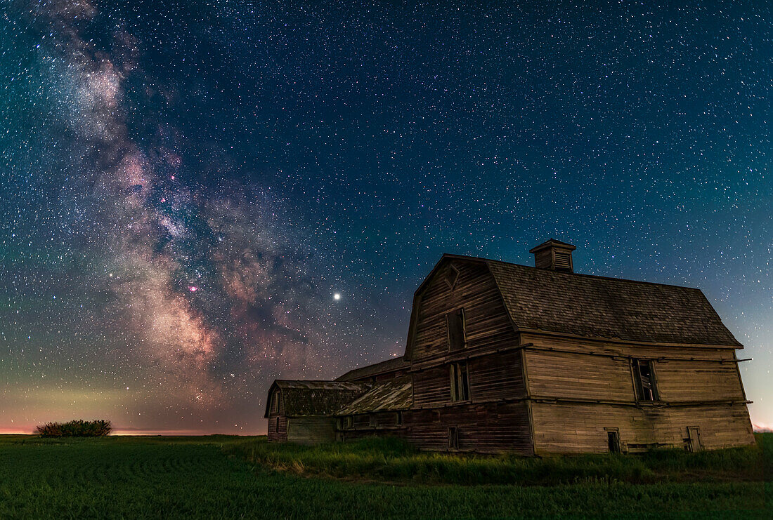 Der Bereich des galaktischen Zentrums der Milchstraße im Sternbild Schütze hinter der großen alten Scheune in der Nähe des Hauses in Süd-Alberta, am 30. Juni 2019. Die Scheune wird von der Dämmerung im Norden beleuchtet, aber auch von der Lichtverschmutzung, die aus dem Westen (rechts im Bild) kommt. Der Himmel ist blau von der ewigen Sommerdämmerung zu dieser Zeit des Jahres.