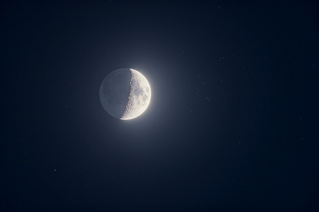 Die 5 Tage alte abnehmende Mondsichel in der Nähe des Sternhaufens Messier 44 im Krebs am Abend des 10. Mai 2019 vor dem Hintergrund des tiefblauen Dämmerungshimmels und mit noch sichtbarem Erdschein auf der dunklen Seite des Mondes.