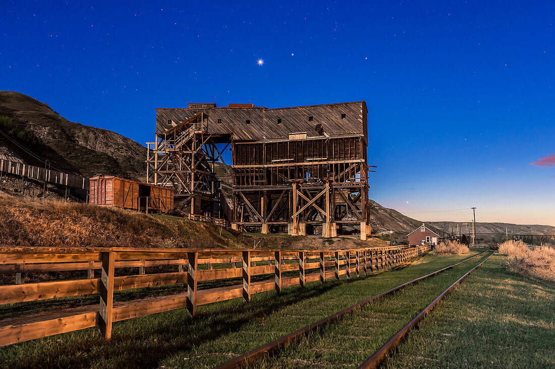 Venus, sehr hell wie ein Abendstern, leuchtet über der alten historischen Atlas-Kohlenmine im Red Deer River Valley, Alberta, in der Nähe von East Coulee. Die Minengebäude sind die letzten Überbleibsel der vielen Kohleminen, die bis in die 1970er Jahre im Tal betrieben wurden. Die Atlas Coal Mine ist heute ein Museum und eine National Historic Site.
