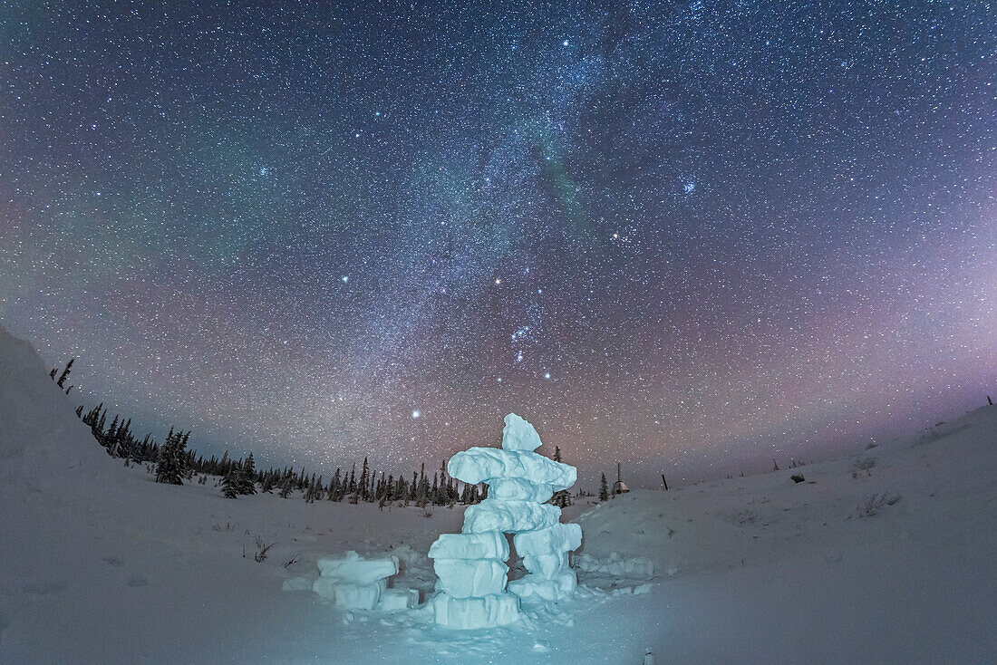 Orion, die Wintersterne und die Milchstraße über einer aus Schneeblöcken gefertigten Inukshuk-Figur im Churchill Northern Studies Centre, Manitoba. Die menschliche Figur des Inukshuks spiegelt die Figur des Orion am Himmel wider. Dies ist eine Einzelbelichtung mit dem 12-mm-Vollformat-Rokinon-Fischaugenobjektiv und der Nikon D750. Der Inukshuk ist mit einem weißen LDE-Scheinwerfer bemalt.