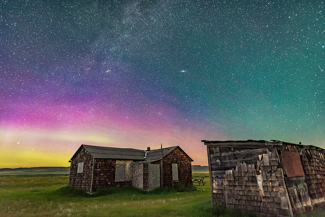 Ein schwaches Polarlicht im Norden des Grasslands National Park, Saskatchewan, bei der Larson Ranch und ihren rustikalen Pionierhütten. Aufgenommen am 8. August 2016. Der Blick geht nach Nordosten in Richtung Andromeda (die Andromeda-Galaxie ist oben in der Mitte) und Perseus (der Doppelhaufen ist links von der Mitte). Dieser Park ist ein Dark Sky Preserve. Es sind keine Lichter sichtbar. Die Beleuchtung erfolgt hier durch das Sternenlicht und die untergehende zunehmende Mondsichel im Südwesten.
