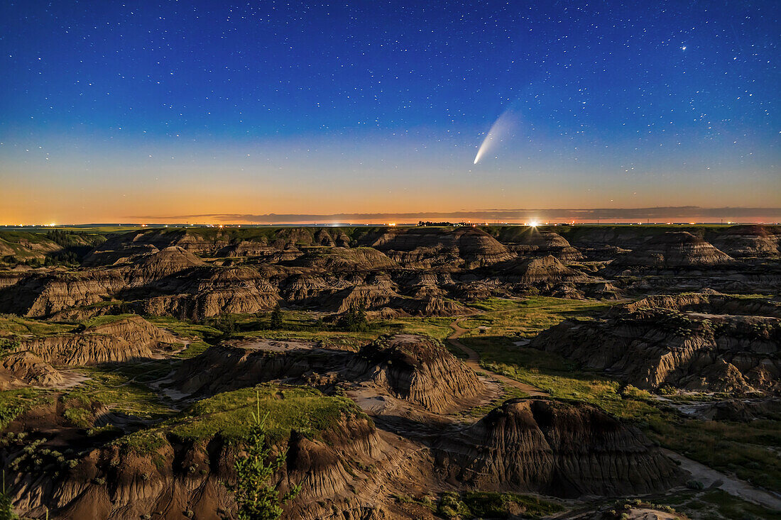 This is Comet NEOWISE (C/2020 F3) over the Horseshoe Canyon formation near Drumheller, Alberta on the night iof July 10-11, 2020, taken about 2 a.m. MDT with the comet just past lower culmination with it circumpolar at this time. Warm light from the rising waning gibbous Moon provides the illumination. The comet’s faint blue ion tail is just barely visible even in the moonlit sky and low altitude. The glow of summer perpetual twilight at latitude 51.5° N still colours the northern horizon despite this being close to the middle of the night.