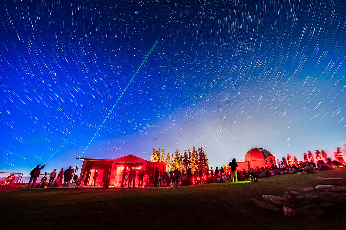 Ein Kompositbild, das mich (rechts, grün beleuchtet) und andere Mitglieder des Calgary RASC Astronomie-Clubs zeigt, die mit grünen Laserpointern auf Polaris zeigen, bei einer öffentlichen Sternenparty am 27. Juli 2019 im Rothney Astrophysical Observatory. An diesem Abend nahmen etwa 600 Personen teil. Ich habe eine lasergeführte Tour durch den Nachthimmel präsentiert.