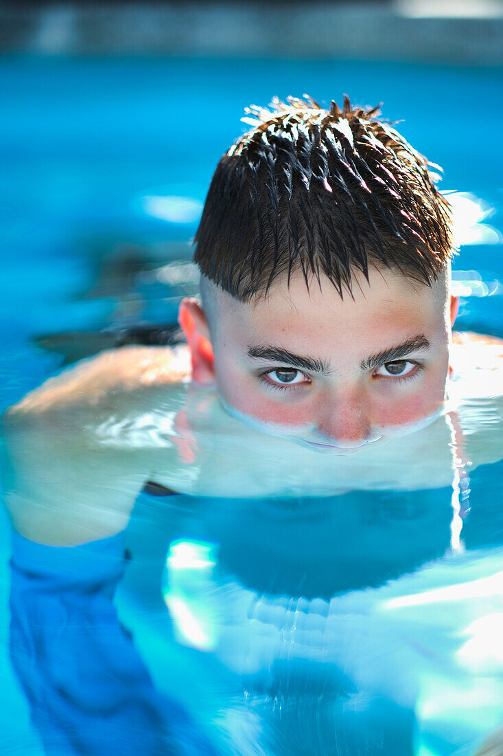 Portrait of a young caucasian boy inside a swimming pool, submerged in water up to his nose. Lifestyle concept.