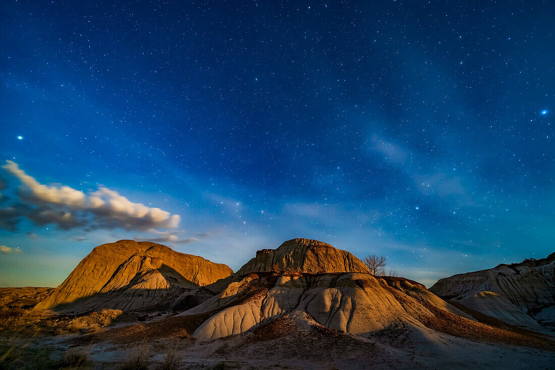 The eroding formations of Dinosaur Provincial Park, Alberta, lit by the rising gibbous Moon, off camera at right, on April 21/22, 2019. This is looking north, with Polaris at upper centre, Capella setting at left, Vega rising at right, and the W of Cassiopeia at lower centre.