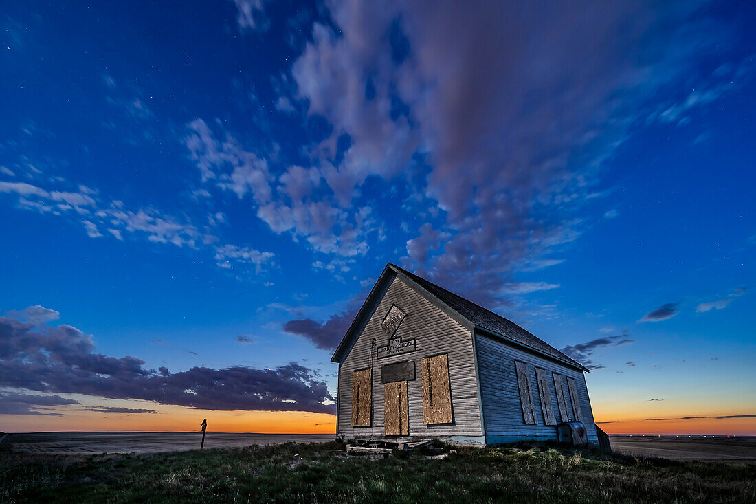 Das Liberty Schoolhouse von 1910, ein klassisches einräumiges Schulhaus der Pioniere in der Prärie von Alberta, bei Sonnenuntergang, wenn die Sterne auftauchen, und mit der Venus links in den Wolken. Das Mondlicht des zunehmenden Mondes sorgt für die Beleuchtung.